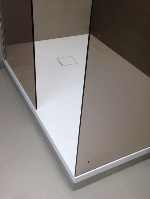 Une cabine de douche avec une base blanche et des portes en verre marron.