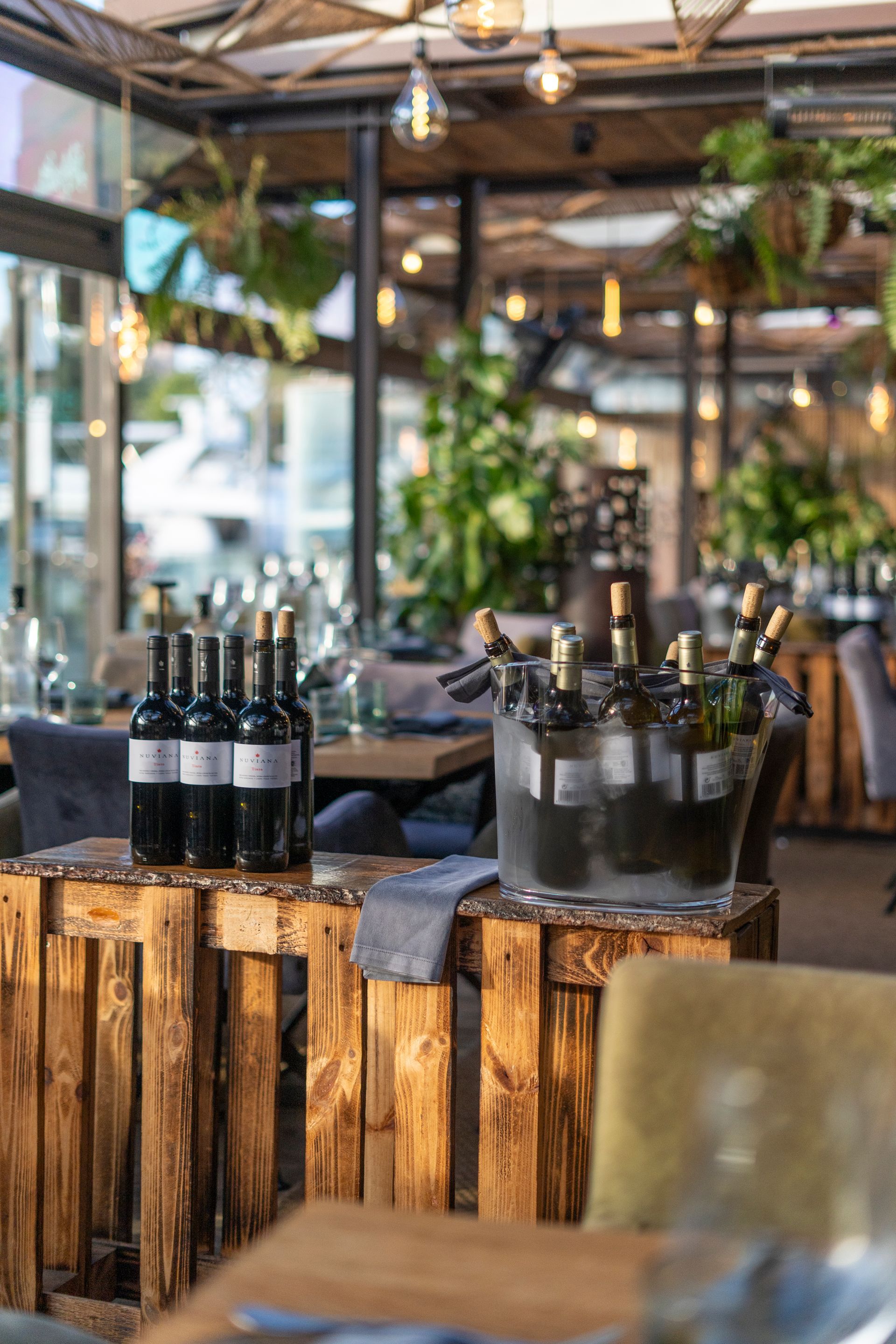 Bottles of wine are lined up on wooden tables in a restaurant