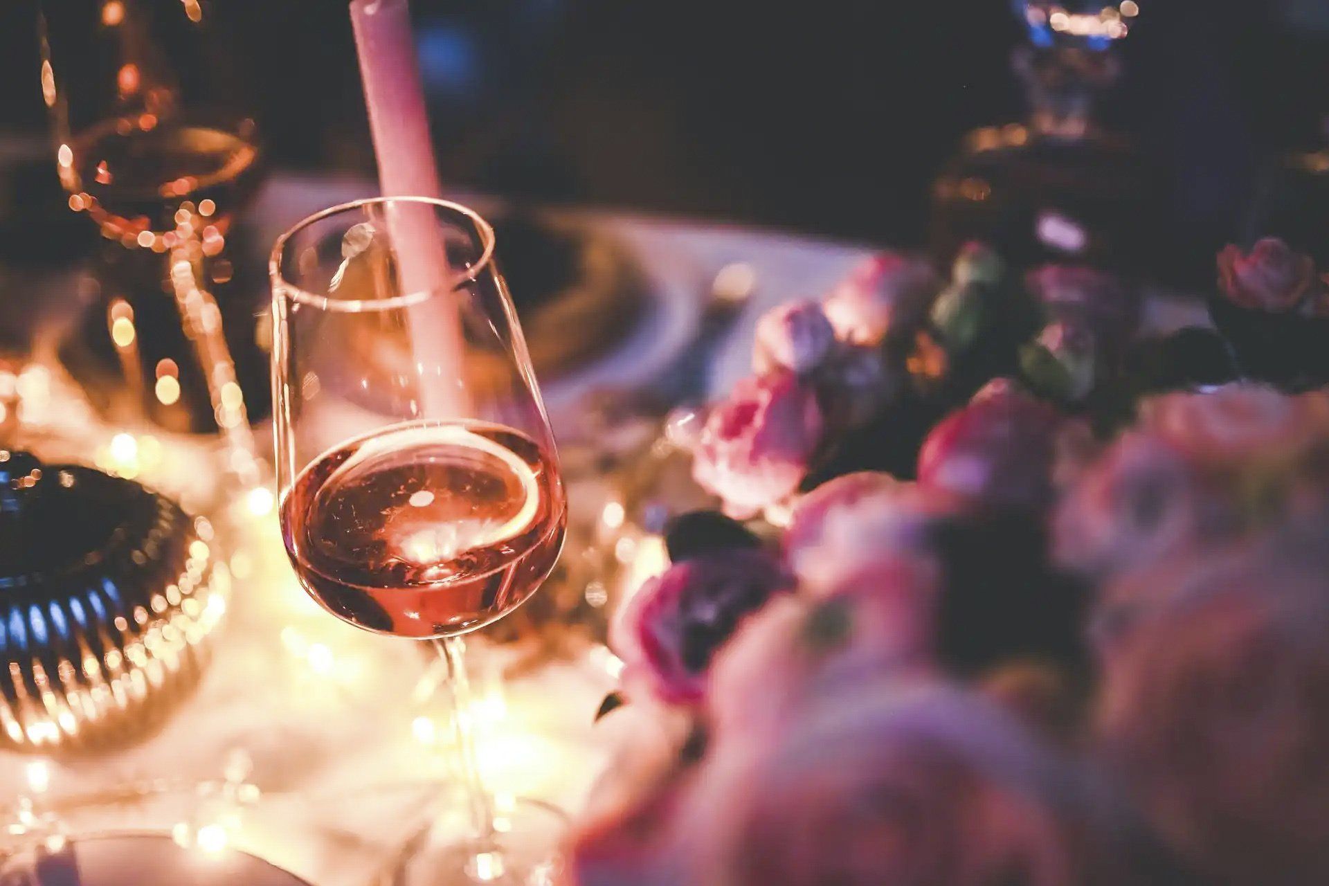 A glass of wine sits on a table with flowers in the background