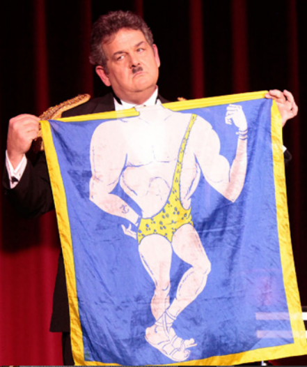 A man in a tuxedo is holding a blue and yellow scarf with a picture of a man in a bathing suit
