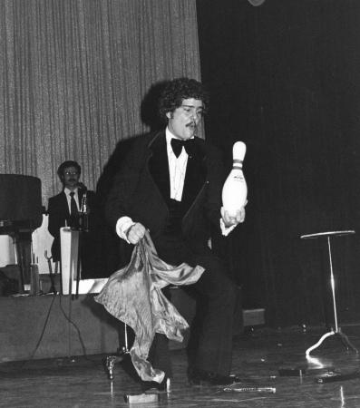 A man in a tuxedo is juggling a bowling pin