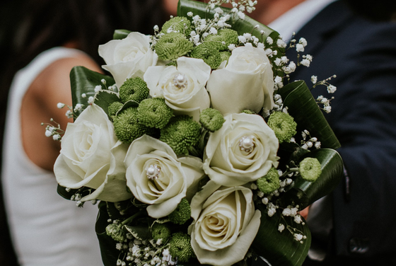 A bride and groom are holding a bouquet of white roses and green flowers.