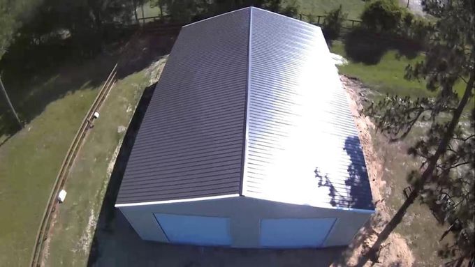 Aerial view of a white metal-roofed building surrounded by trees and grass.
