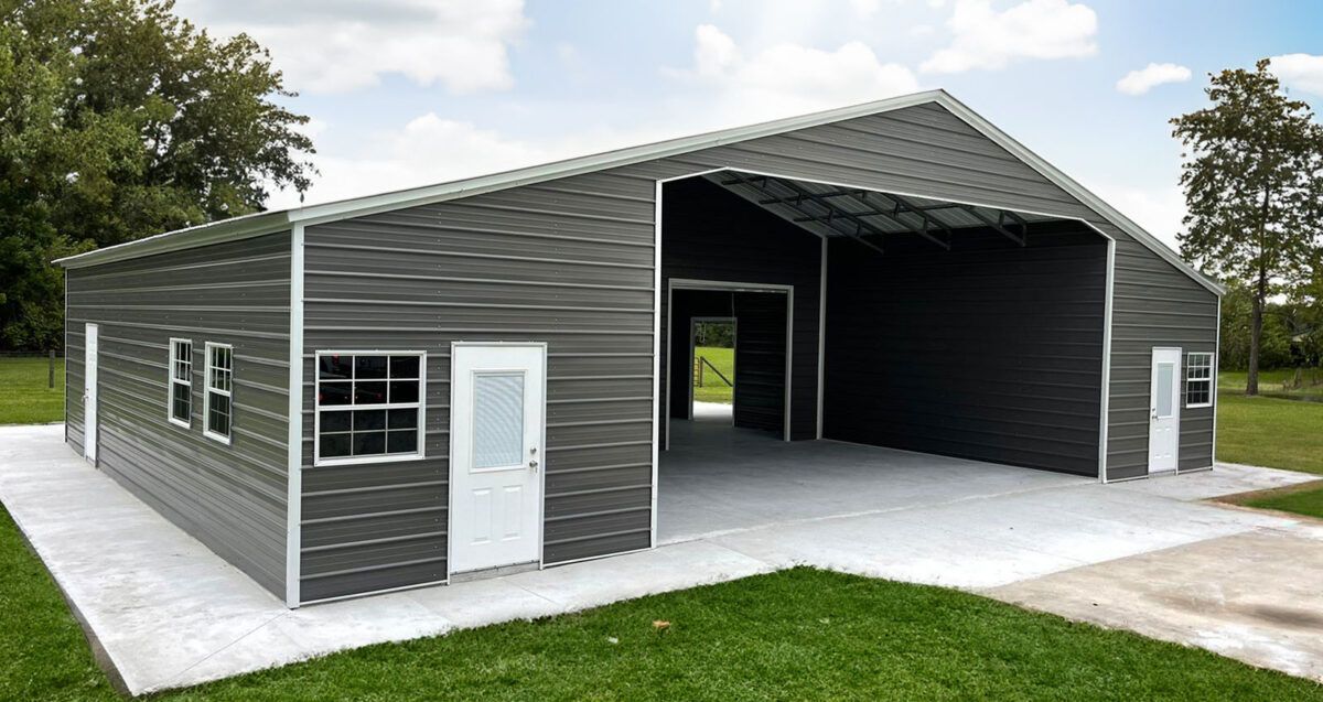 Gray metal garage or workshop building with large open bay and white doors on a concrete pad