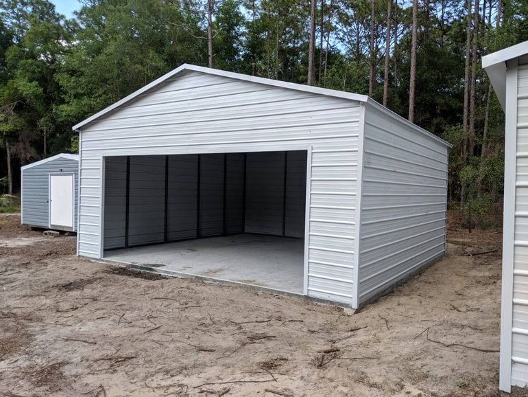 White metal storage shed with a large open garage-style door on a dirt lot.