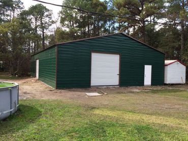 Green metal storage shed with white doors in a wooded yard