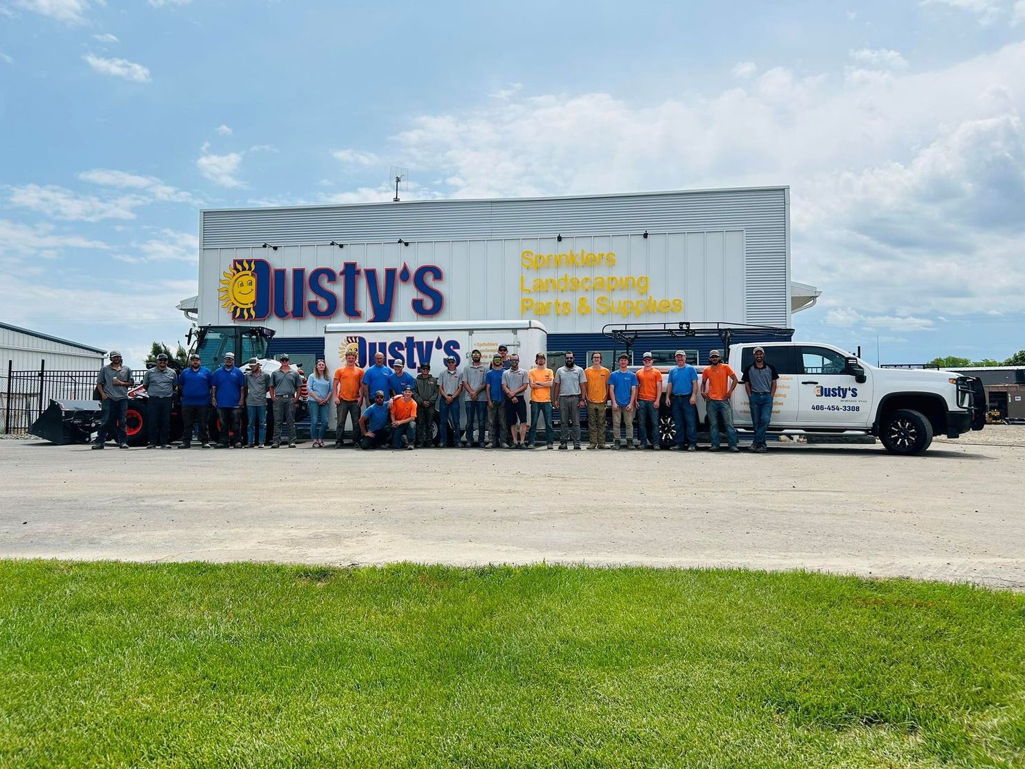 A group of employees stands in front of a Dusty's company building and several service trucks on a sunny day.