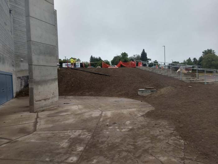 Construction area with a concrete pillar in the foreground, a sloped dirt mound, and orange safety fencing in the distance.