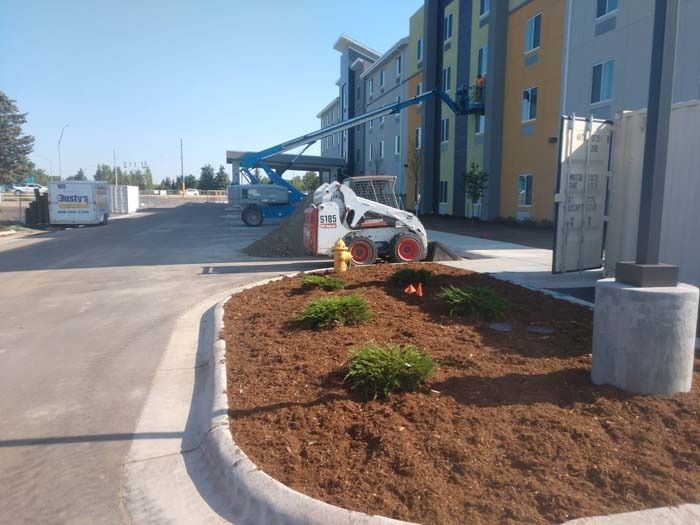 Construction at a hotel with a white skid-steer, a blue boom lift reaching the building, and landscaped mulch beds.