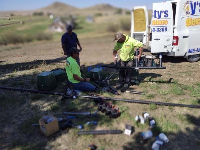 Three technicians work on pipe equipment in a rural, open field next to a white service van.