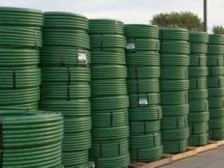 Stacks of coiled green industrial plastic pipes arranged in rows on wooden pallets outdoors.