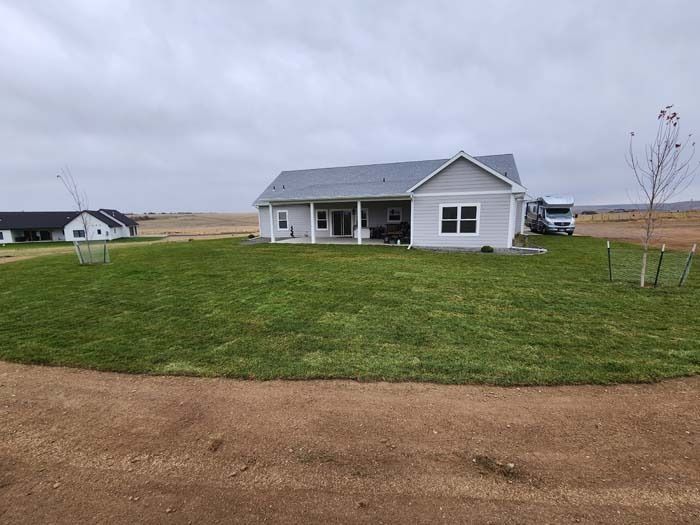 A gray single-story house with a front porch, located on a grassy lot under an overcast sky.