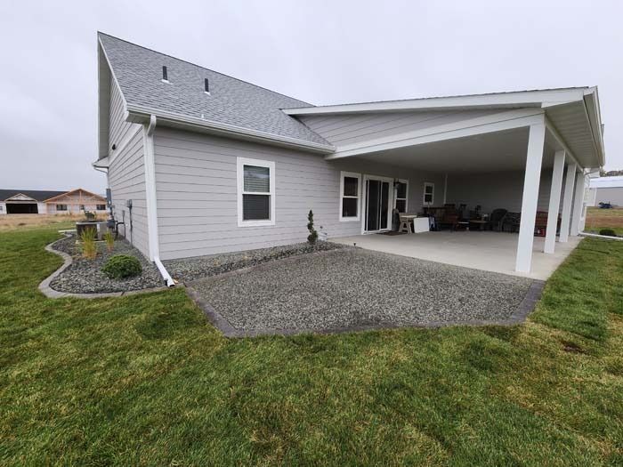 A light grey house with a covered patio, gravel landscaping, and a grassy yard under a cloudy sky.