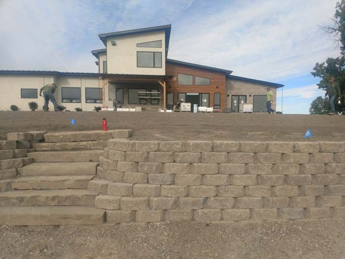 Workers stand before a modern multi-level building with a stone retaining wall and concrete steps in the foreground.