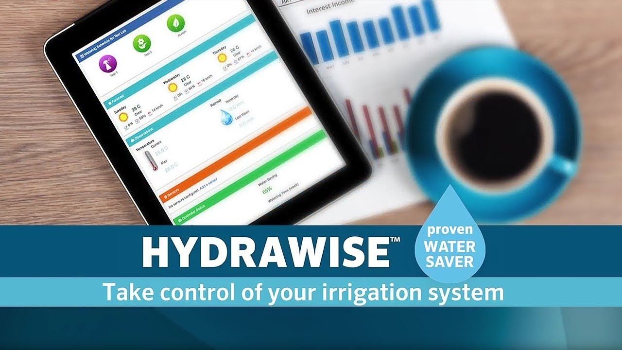 A tablet displays the Hydrawise irrigation dashboard next to a coffee cup and business charts on a wooden desk.