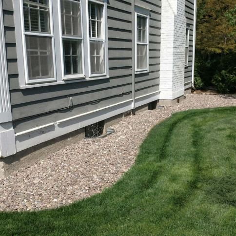 The side of a gray-sided house with a white brick chimney above a gravel landscaping bed and a manicured green lawn.