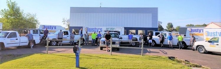 A group of people standing in front of parked company trucks and a warehouse building on a sunny day.