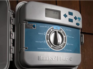 A Hunter Pro-C irrigation controller mounted on a wall with a circular dial and digital display.