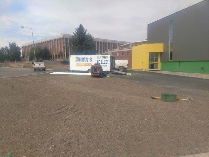 A Dusty's Moving trailer sits on a gravel lot near a building with yellow and green walls under a cloudy sky.