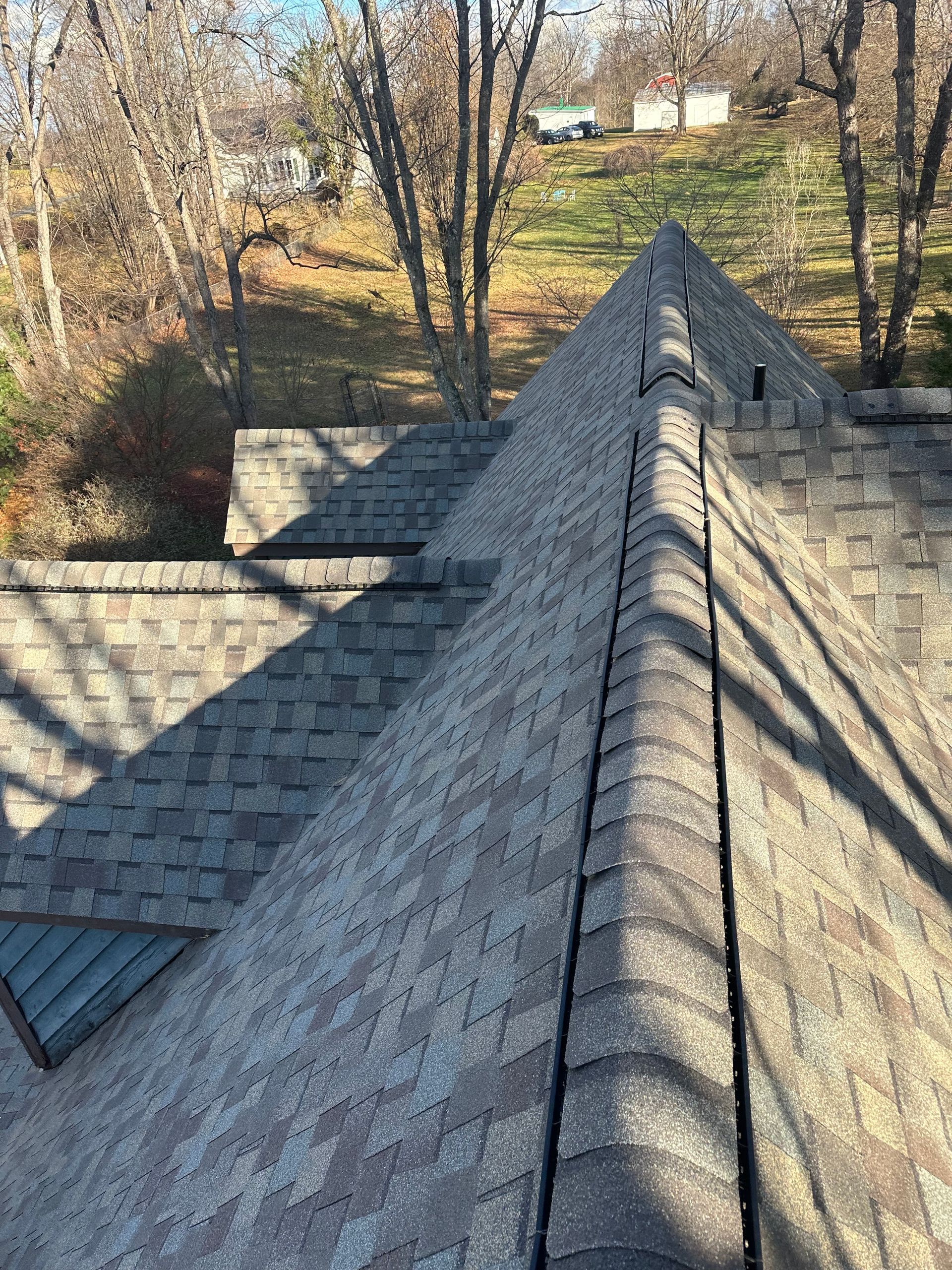 Close-up view of a shingled roof with a peak. Brown and gray shingles in a sunny outdoor setting.