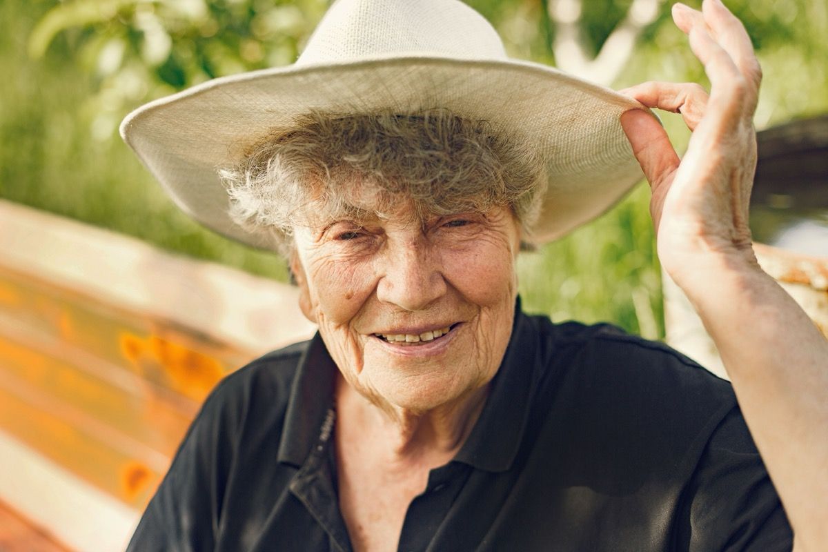 Smiling person in a white hat and black shirt outdoors, holding up the hat brim.