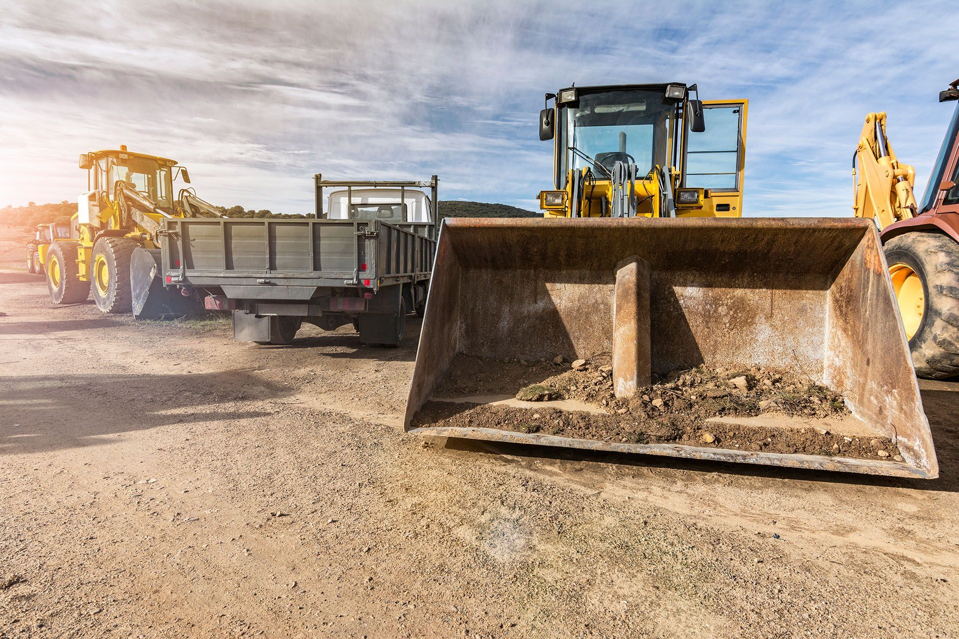 A row of construction vehicles are parked in a dirt lot.