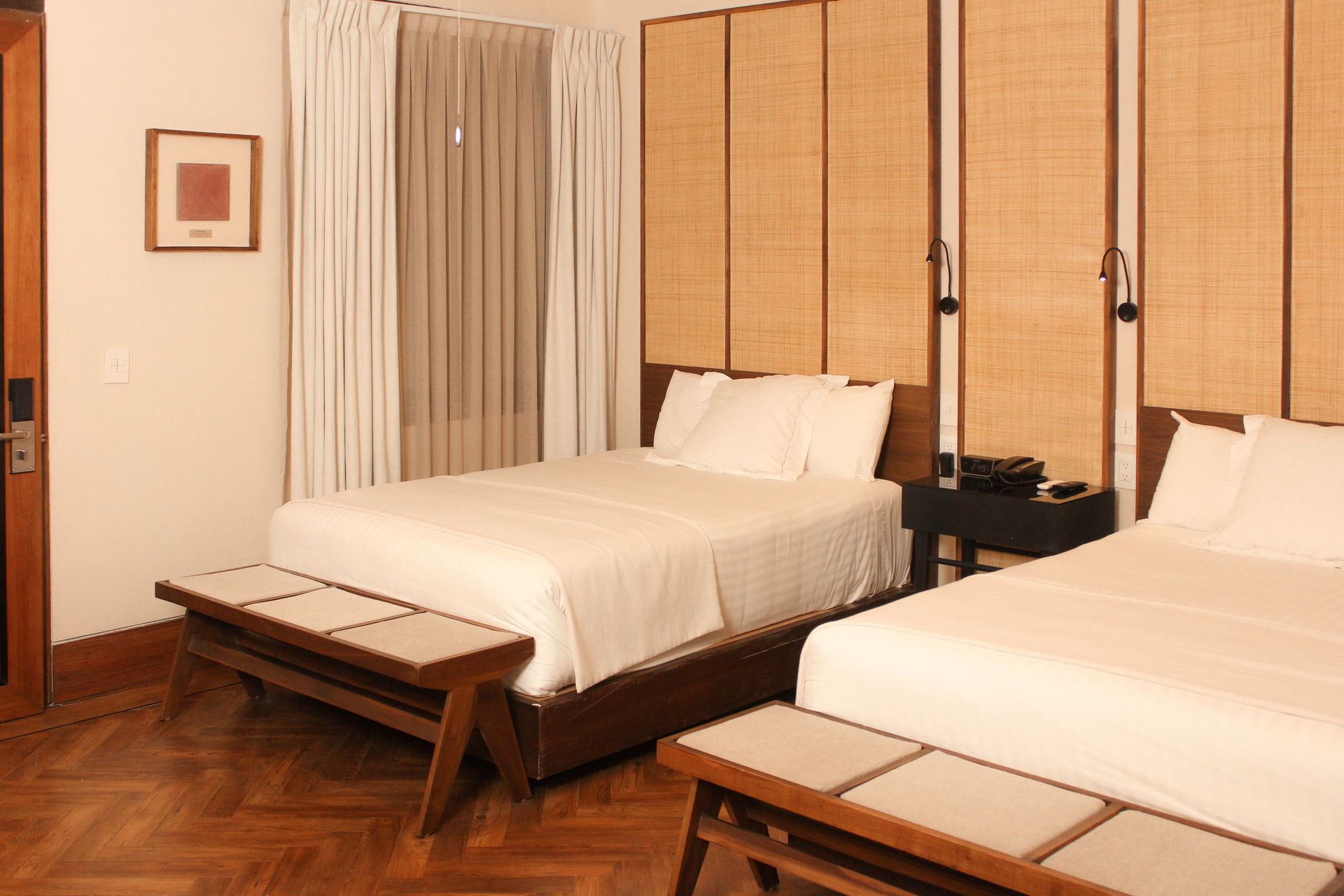 Dos camas impecablemente hechas en una habitación de hotel de tonos cálidos con paneles de bambú en las paredes y cortinas.