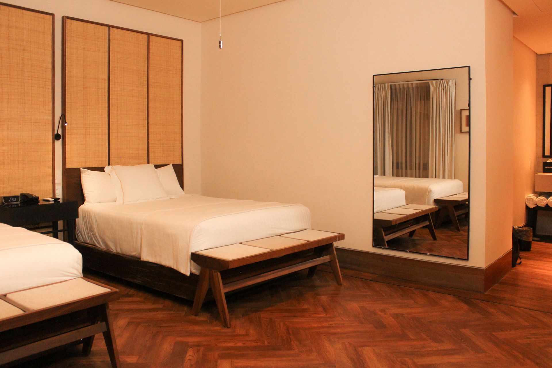 Dormitorio moderno con dos camas, suelo de madera y un espejo de pared que refleja la habitación.