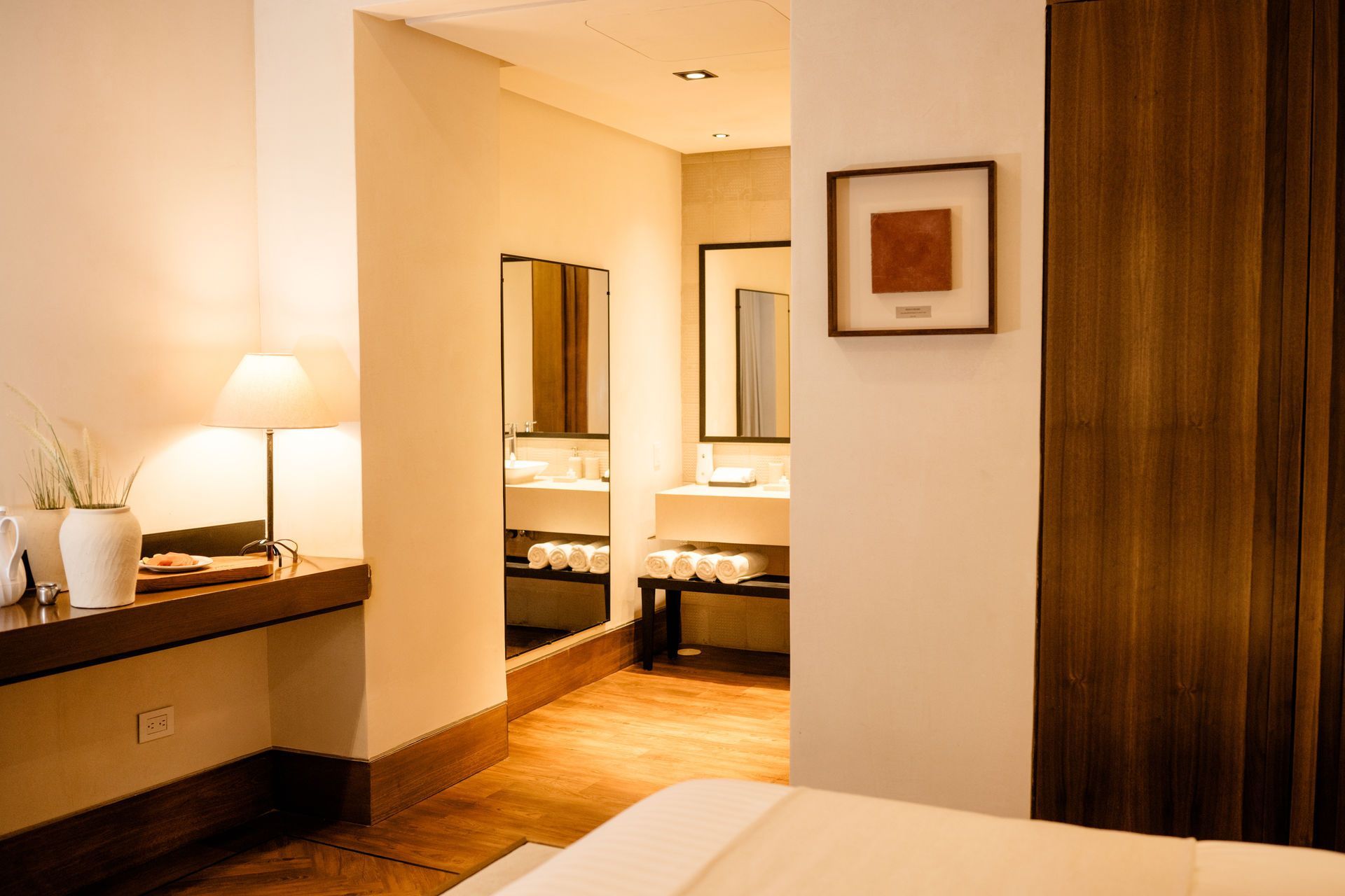 Interior acogedor de una habitación de hotel con cama, lámpara de escritorio, espejos y detalles de madera.