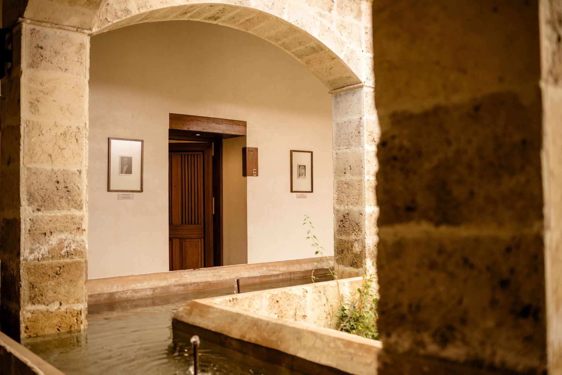 Patio de piedra con pasadizo arqueado, puerta de madera y arte mural enmarcado en luz cálida.