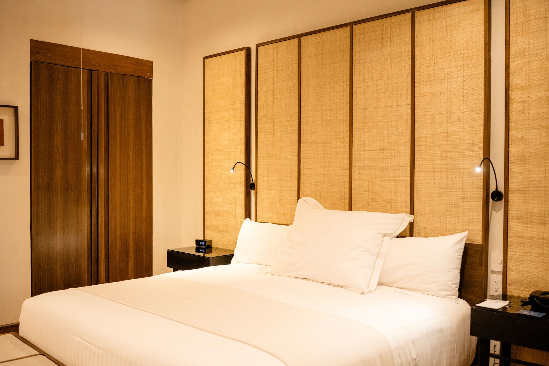 Dormitorio moderno con una cama blanca impecablemente hecha, paneles de pared tejidos y cálidos detalles de madera.