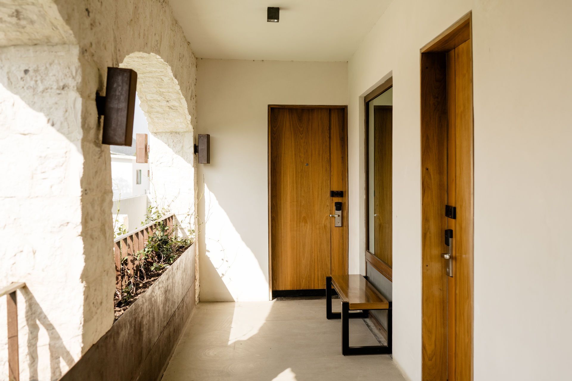 Pasillo de apartamento soleado con dos puertas de madera, arco de piedra y un pequeño banco.