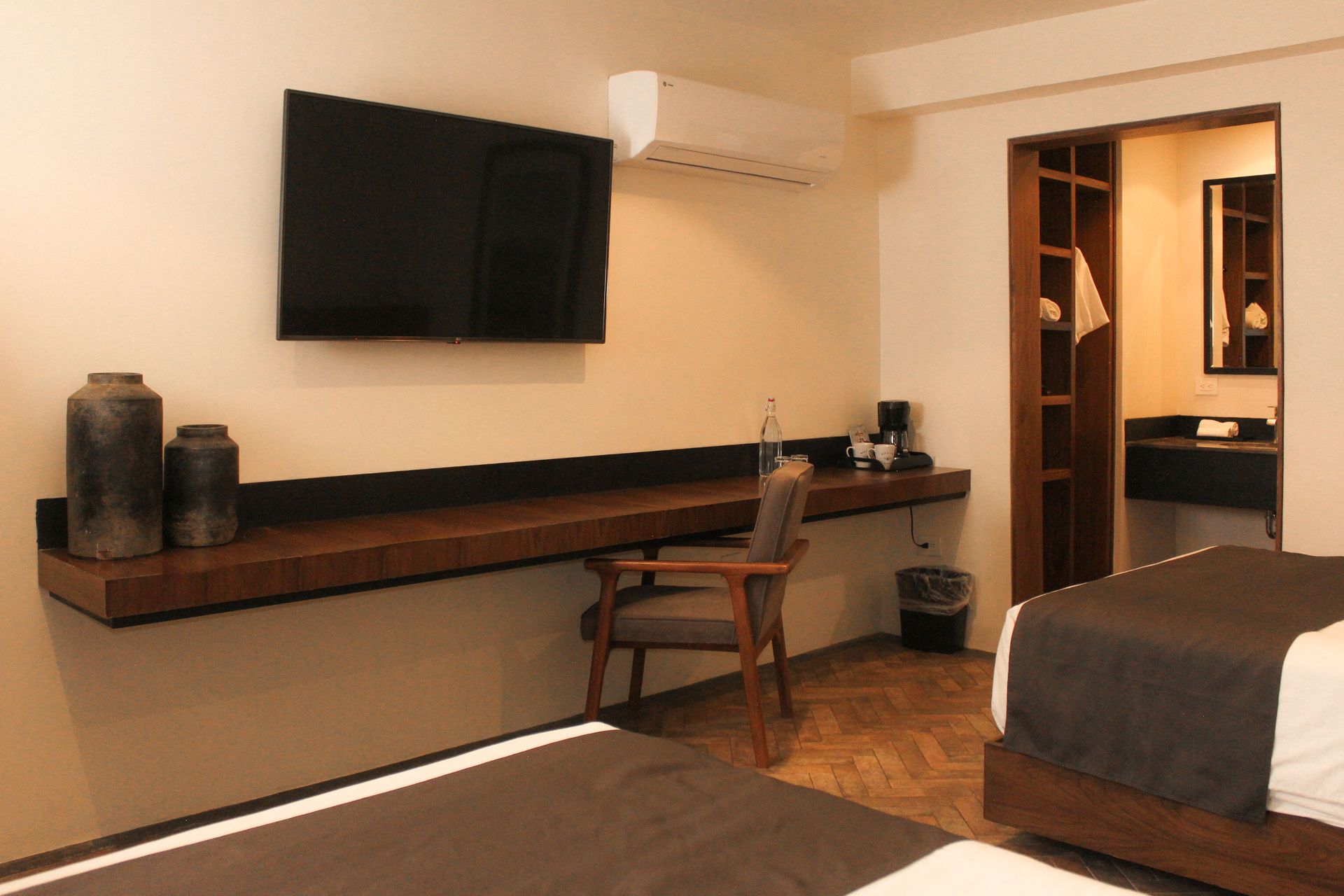 Habitación de hotel con dos camas, televisor montado en la pared, escritorio, silla y puerta abierta que da al baño.