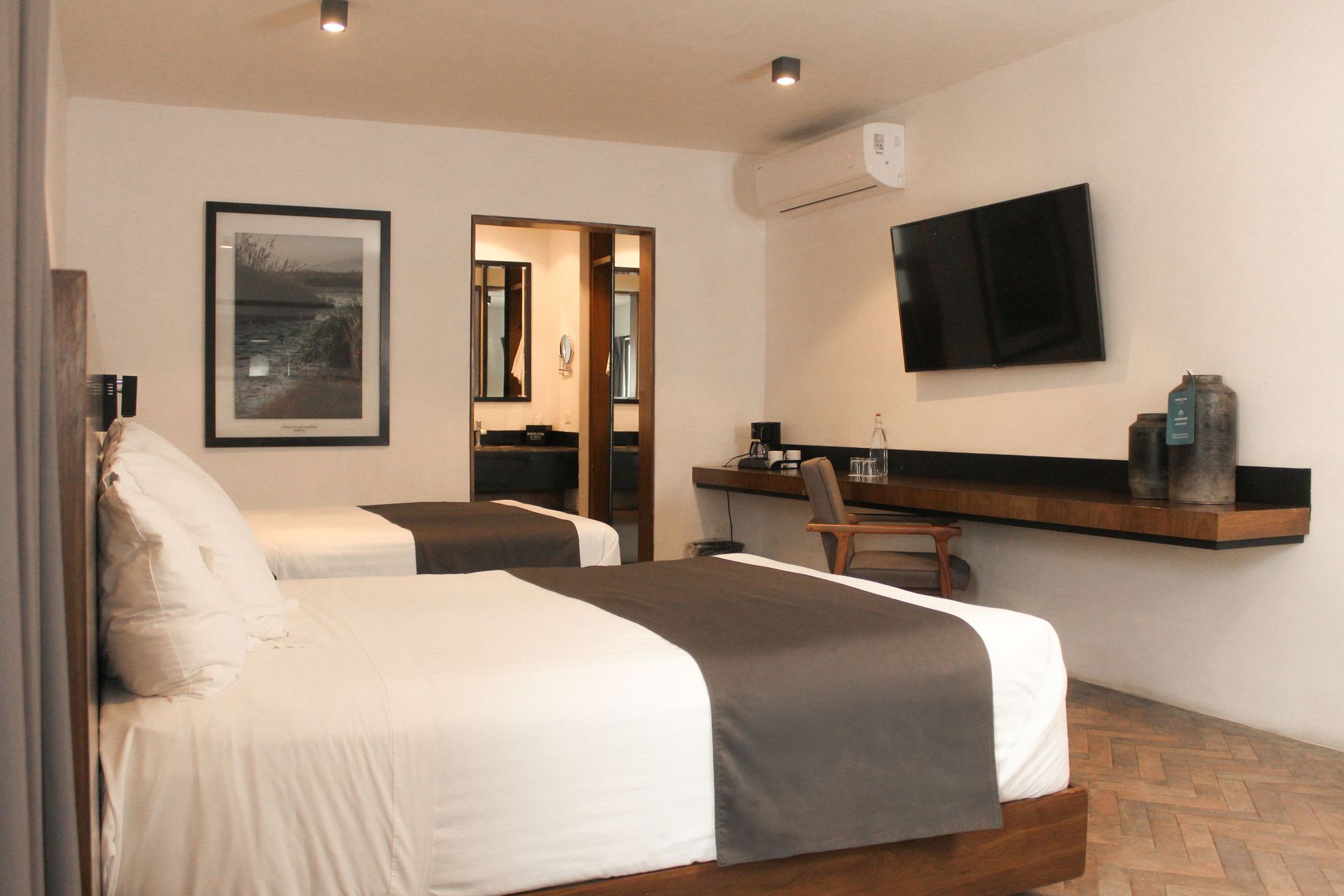 Habitación de hotel minimalista con dos camas blancas, televisor montado en la pared, escritorio .
