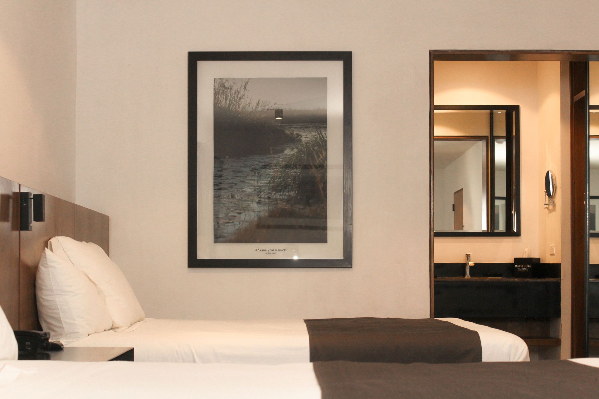 Habitación de hotel con dos camas, cuadros enmarcados en la pared y vista al tocador del baño.