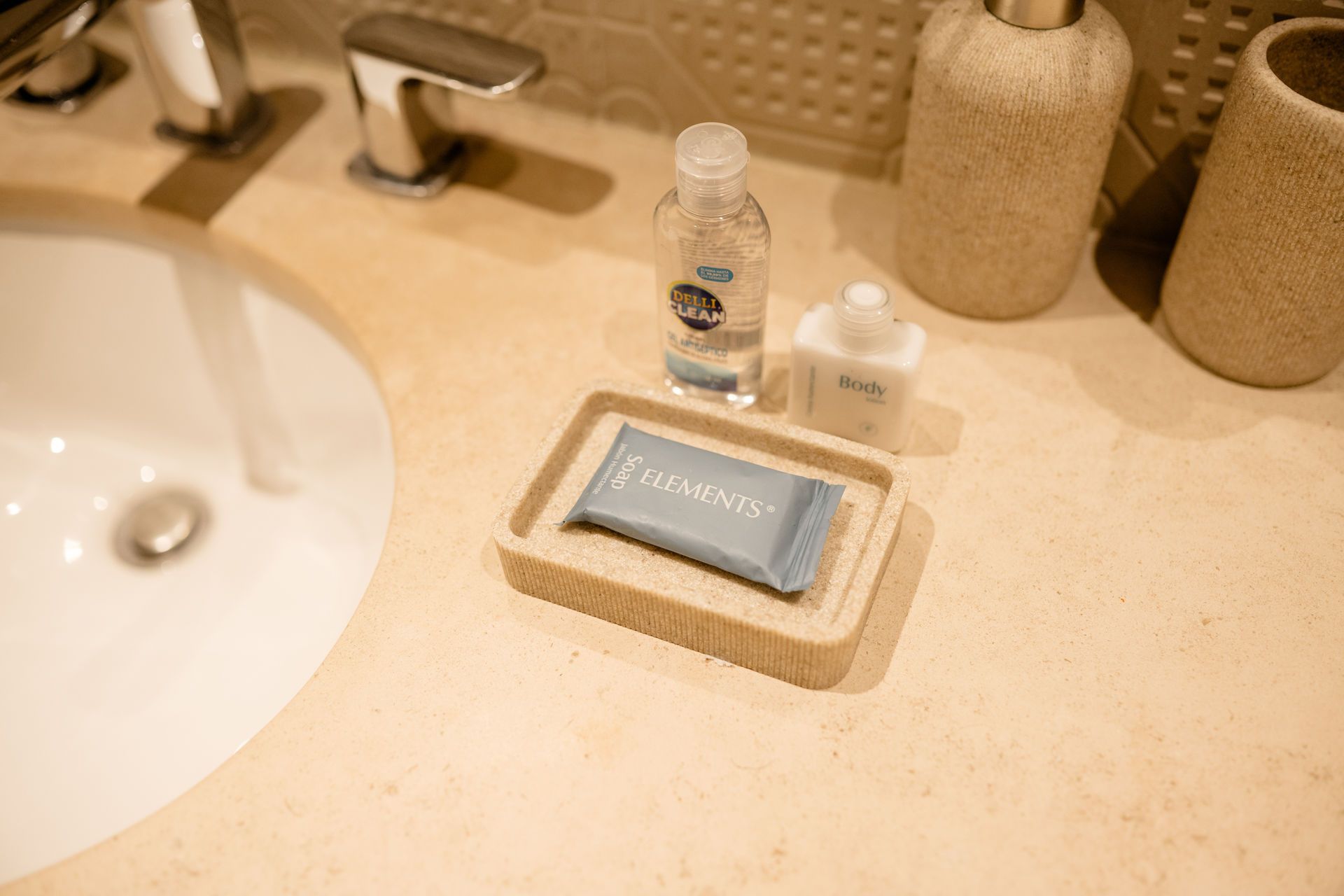 Lavabo de baño con artículos de tocador y jabonera sobre una encimera de color beige.