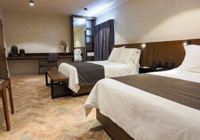 Habitación de hotel con dos camas blancas, suelo de madera, escritorio y cortinas.