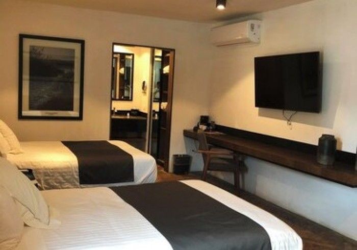 Habitación de hotel con dos camas individuales, televisor montado en la pared, escritorio y puerta de acceso al baño.