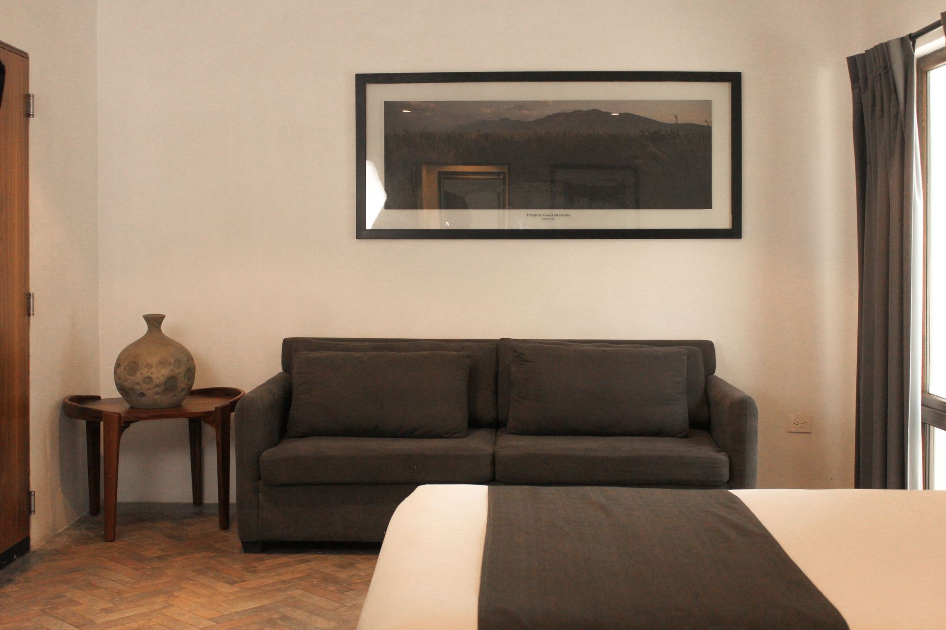 Dormitorio moderno con un sofá oscuro, una mesita auxiliar, cuadros en la pared y una cama en primer plano.