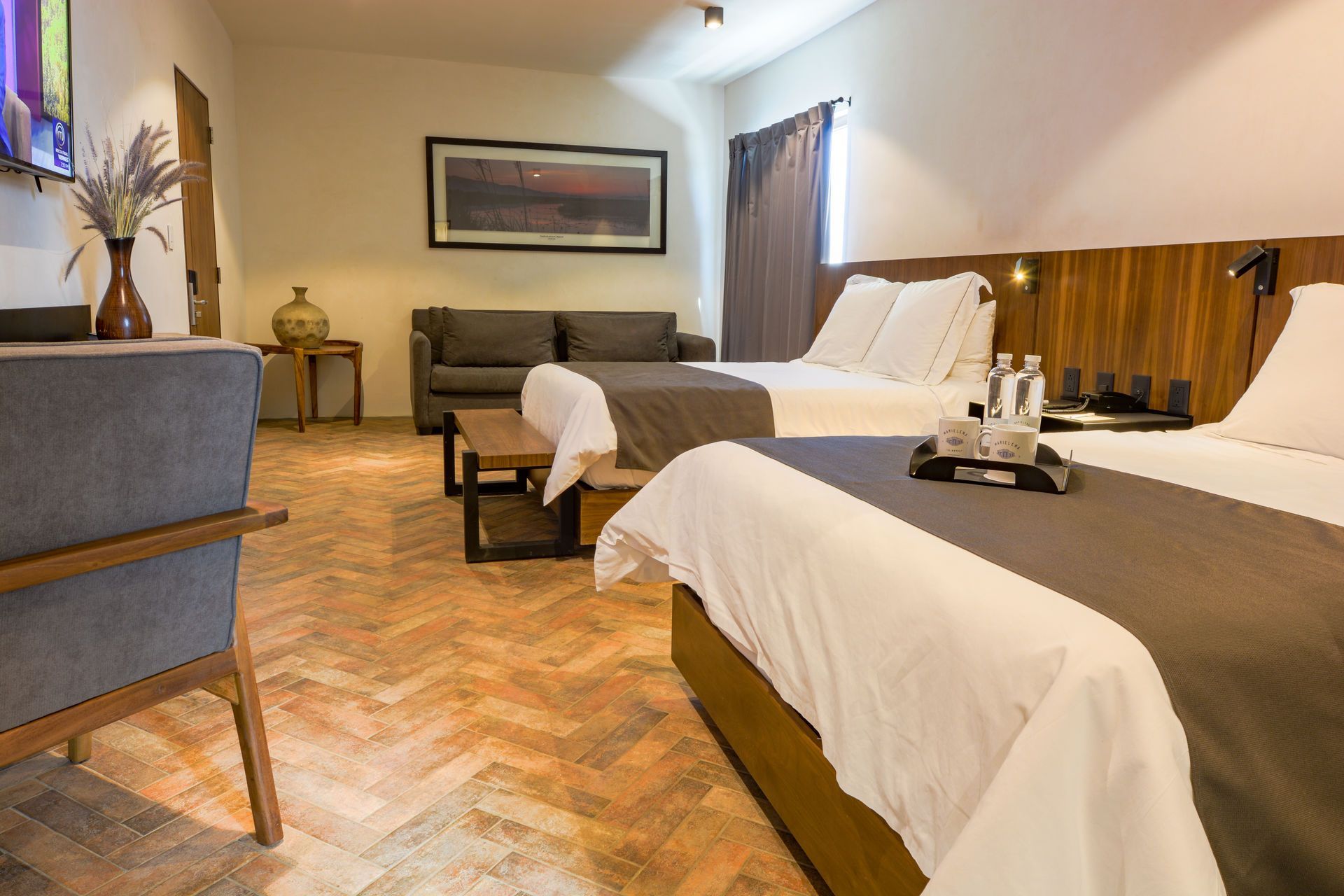 Habitación de hotel con dos camas bien hechas, paneles de madera cálida y una zona de estar junto a la ventana.