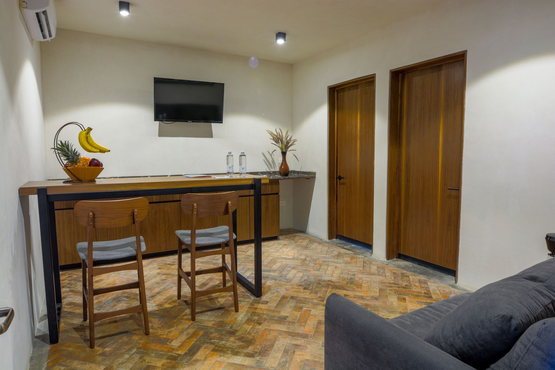 Comedor moderno con dos taburetes de madera, barra, televisor de pared y puertas de madera cerradas.