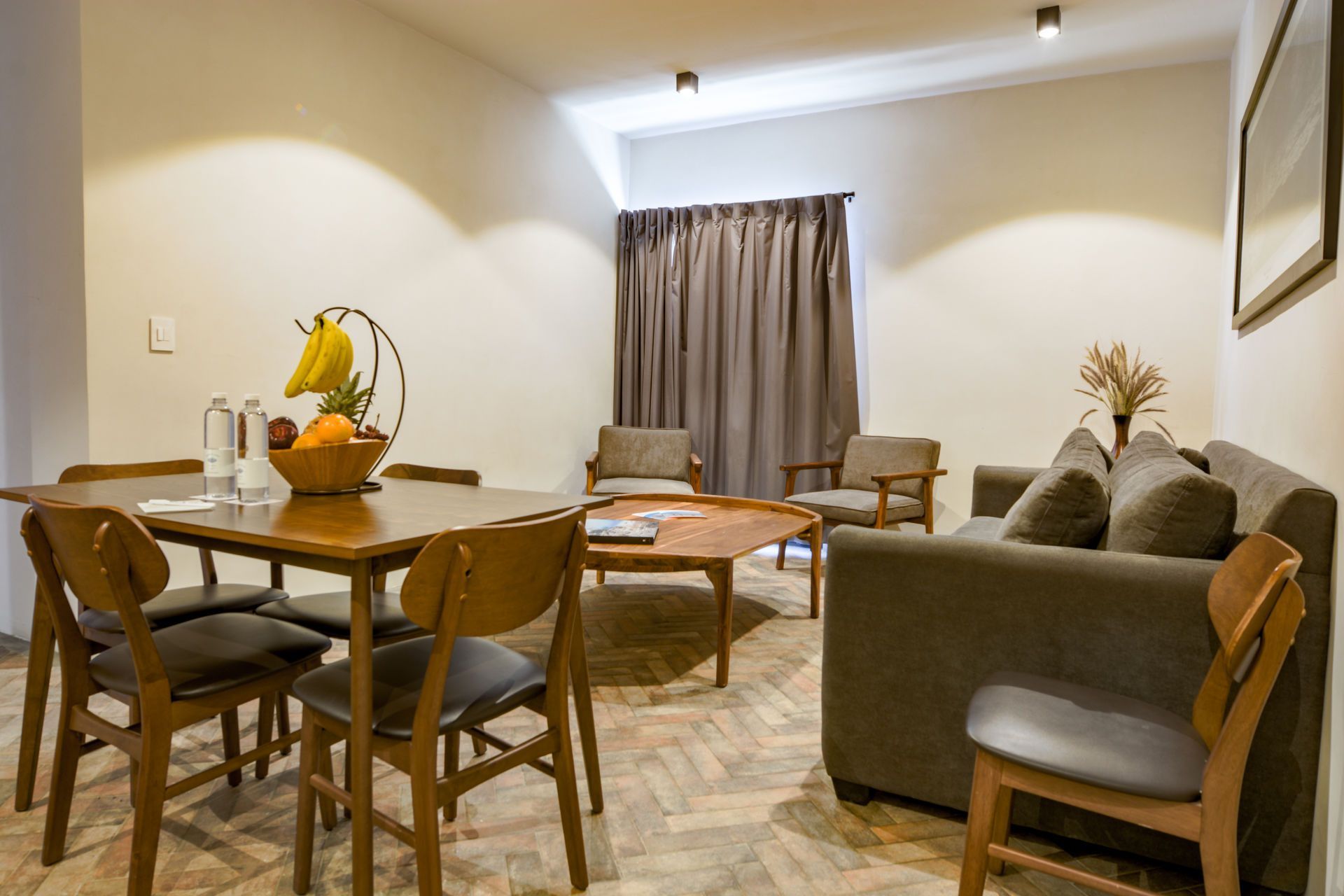 Acogedor salón-comedor con mesa de madera, sillas, sofá gris, mesa de centro, cortinas e iluminación cálida.
