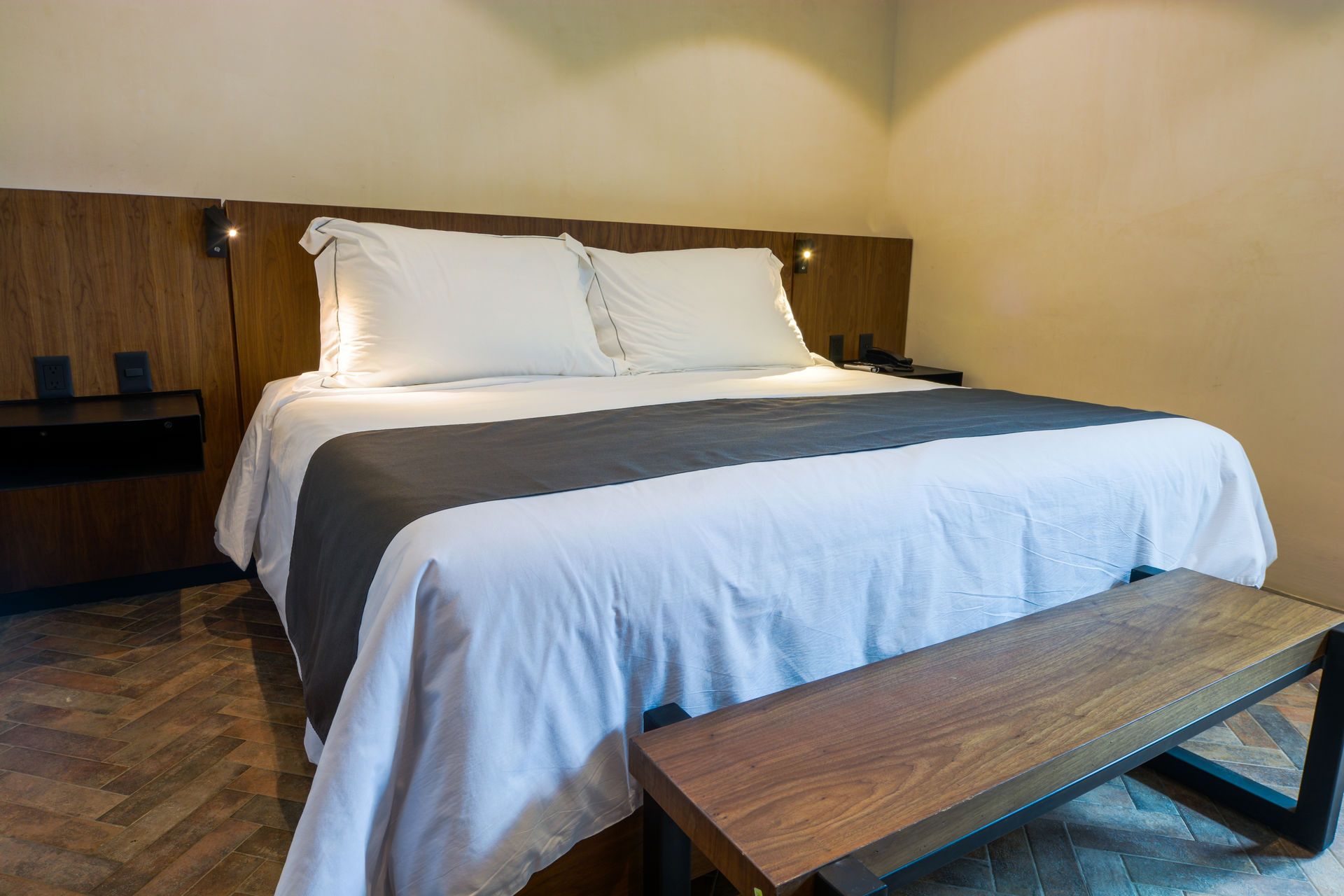 Dormitorio moderno con una cama blanca, cabecero de madera y banco en primer plano.