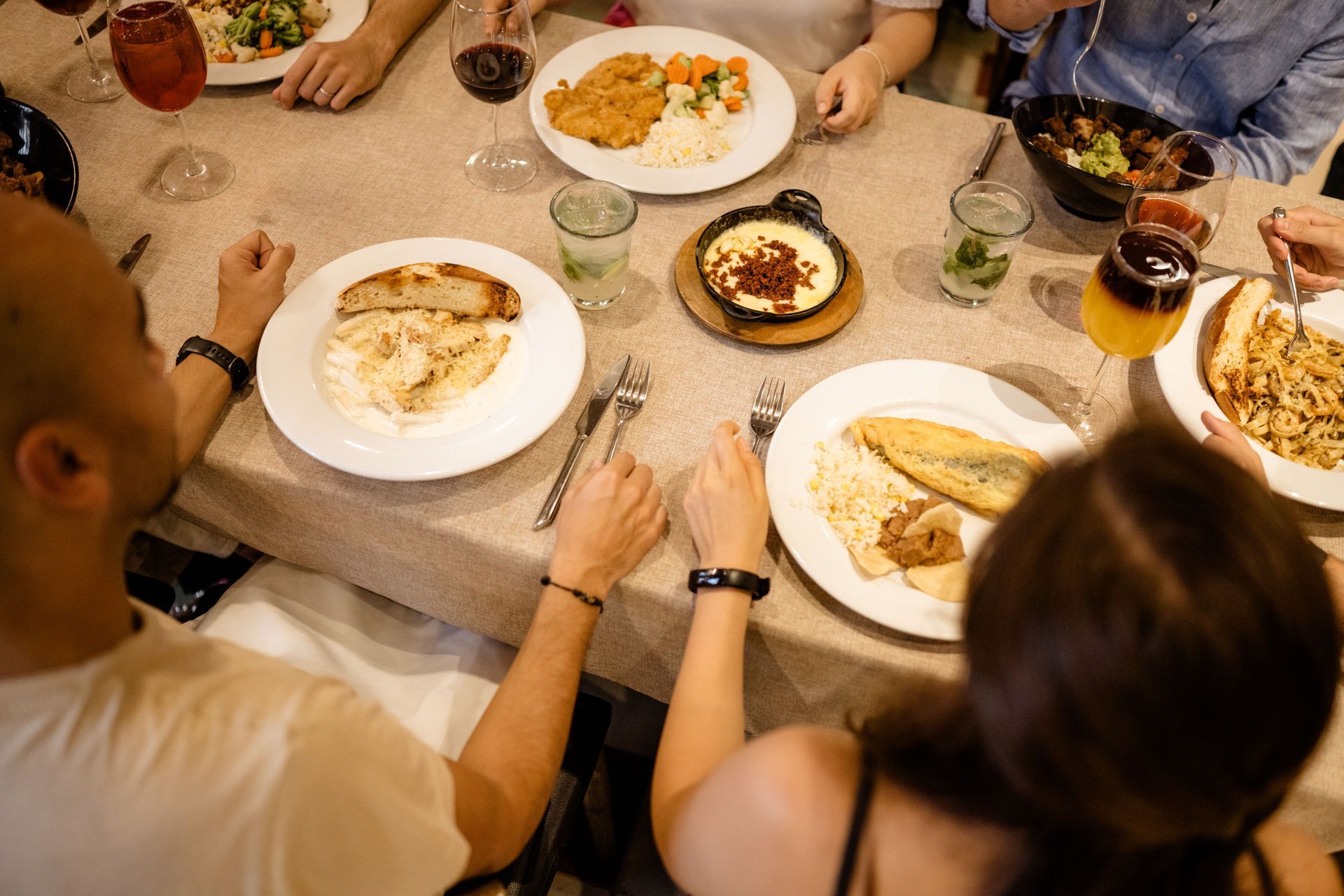 La gente se reunía alrededor de una mesa, compartiendo platos de comida y bebida durante una comida.