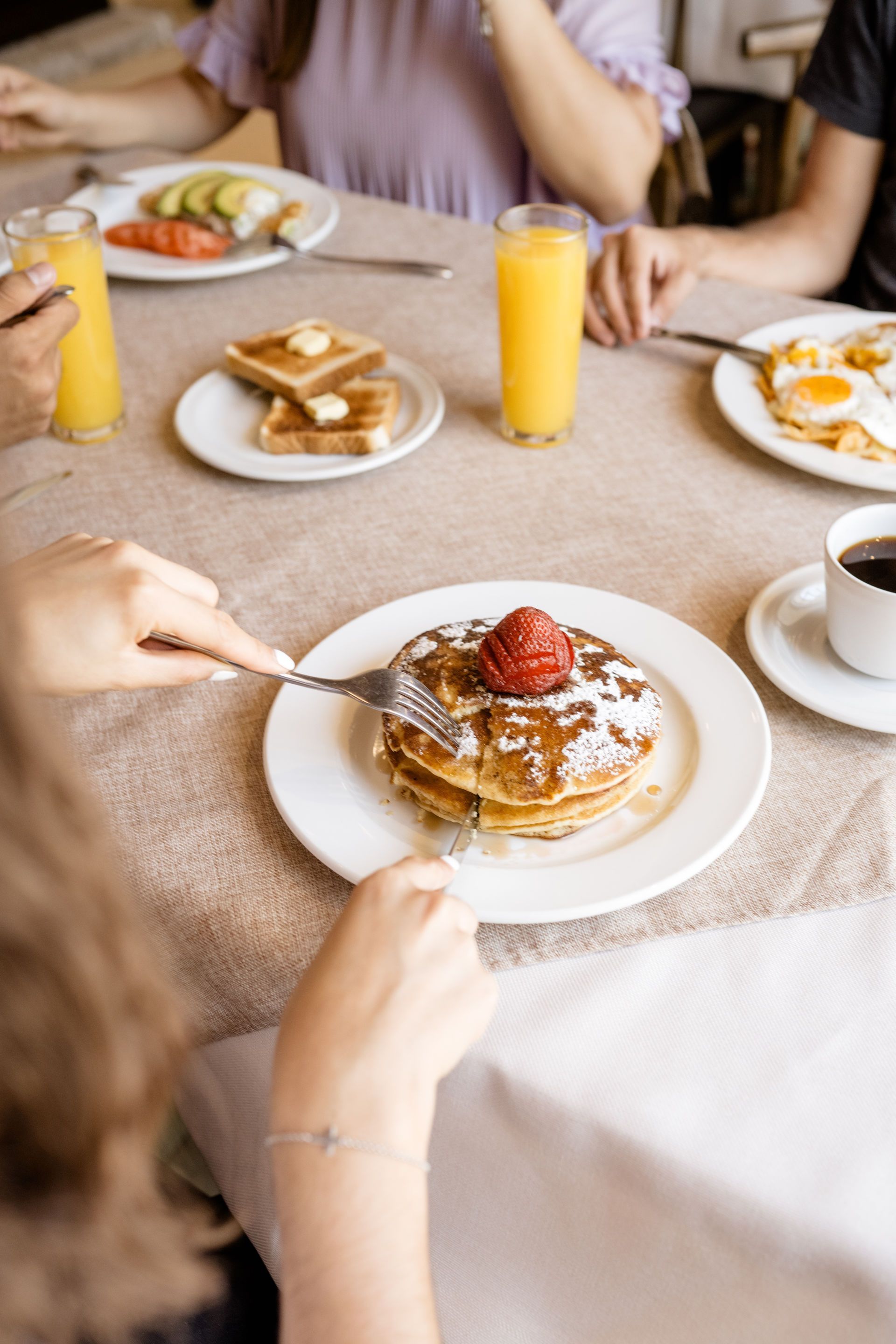 Mesa de brunch con panqueques, huevos, tostadas, jugo de naranja, café y sirope servido a mano.