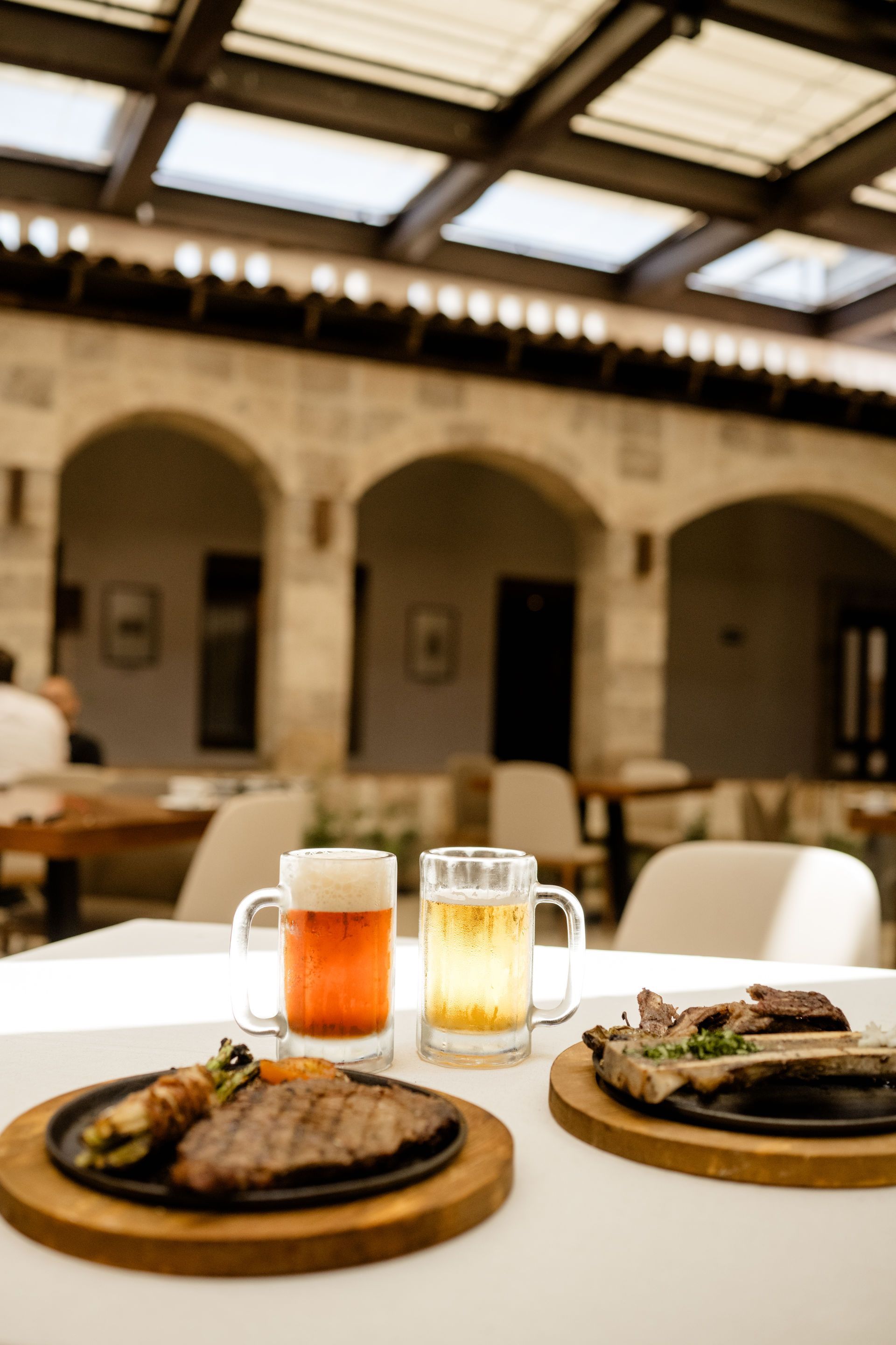 Filetes emplatados y cerveza sobre una mesa en un restaurante con patio soleado.