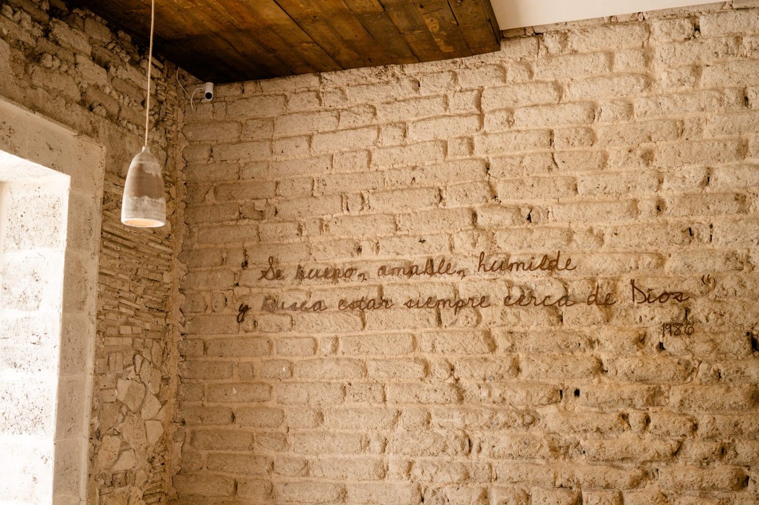 Habitación rústica de ladrillo con una lámpara colgante y texto escrito a mano pintado en la pared.