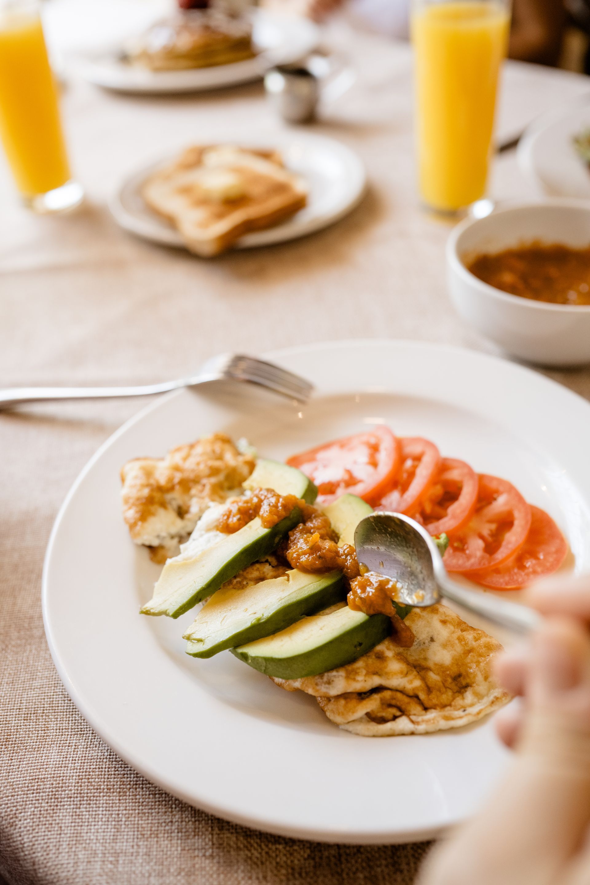 Plato de desayuno con tostada de aguacate, salmón ahumado, huevos y zumo de naranja sobre una mesa.