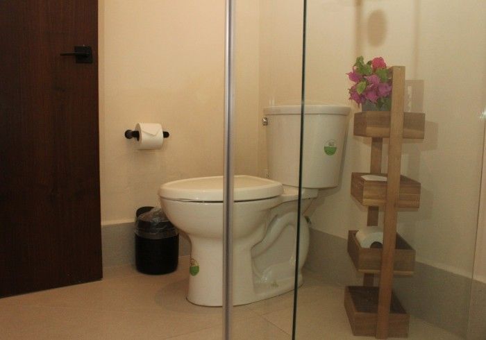 Baño pequeño con inodoro, portarrollos de papel higiénico, papelera y estante de madera