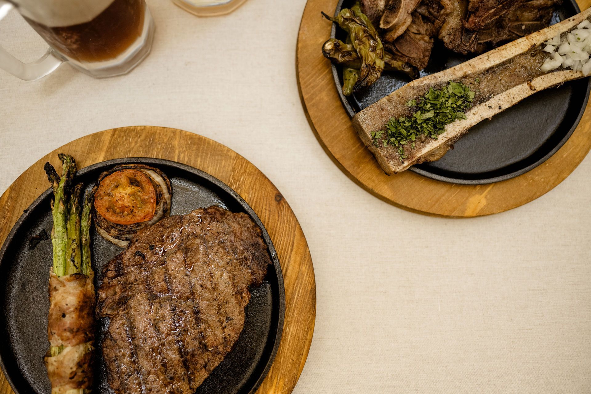 Dos platos con filete a la parrilla, espárragos y una pequeña taza de salsa sobre una mesa clara.